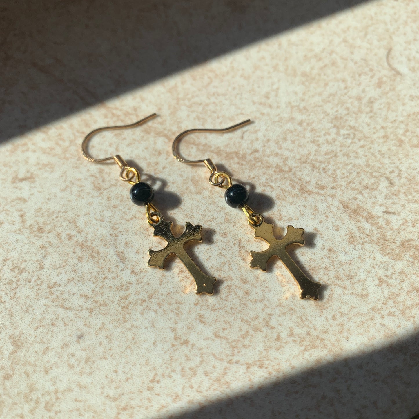 Delicate gold cross drop earrings featuring smooth black beads, perfect for gothic and baroque fashion styles.
