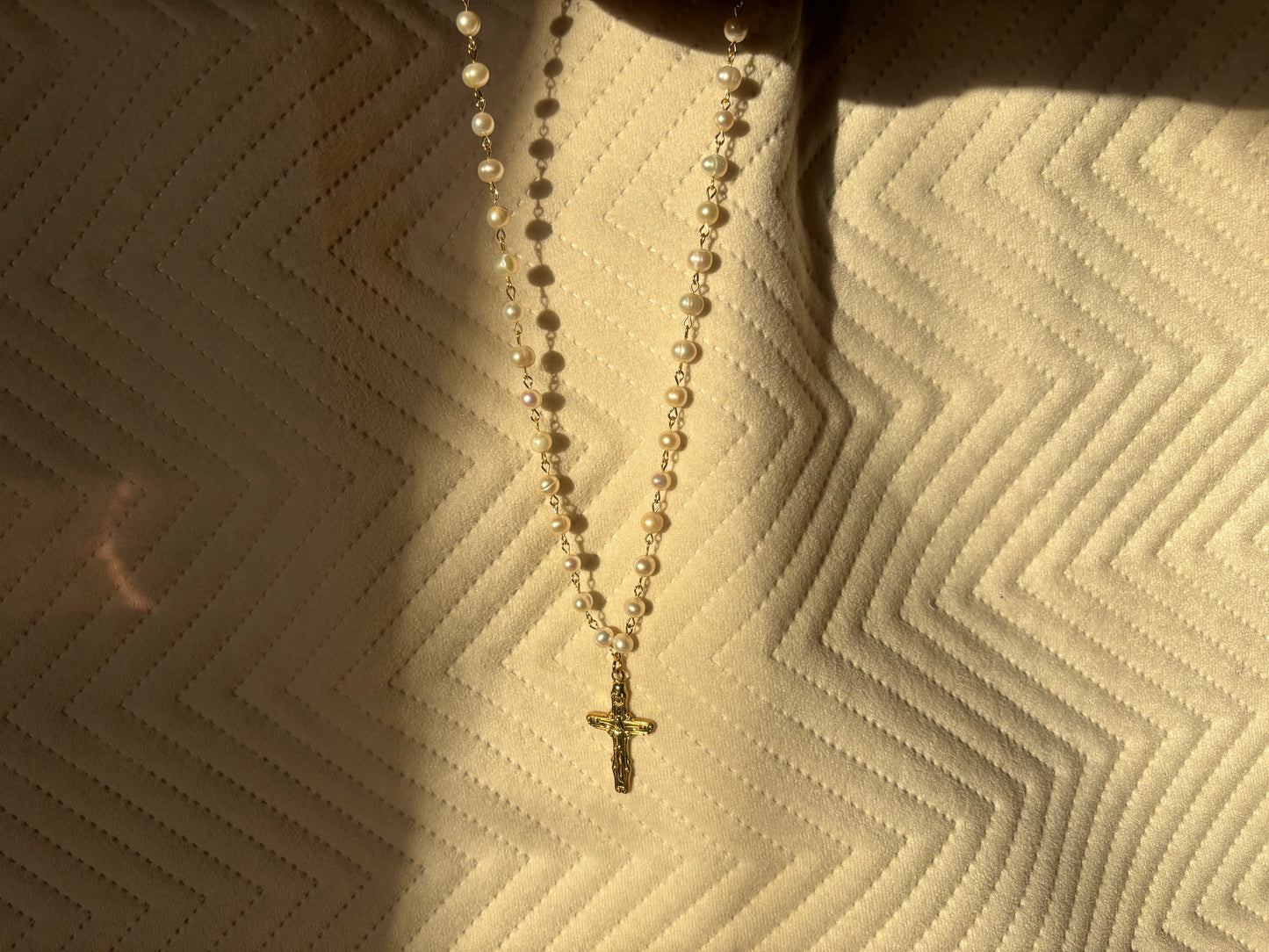 Rosary-like pearl necklace with a gold cross charm, a baroque vintage style jewelry piece.