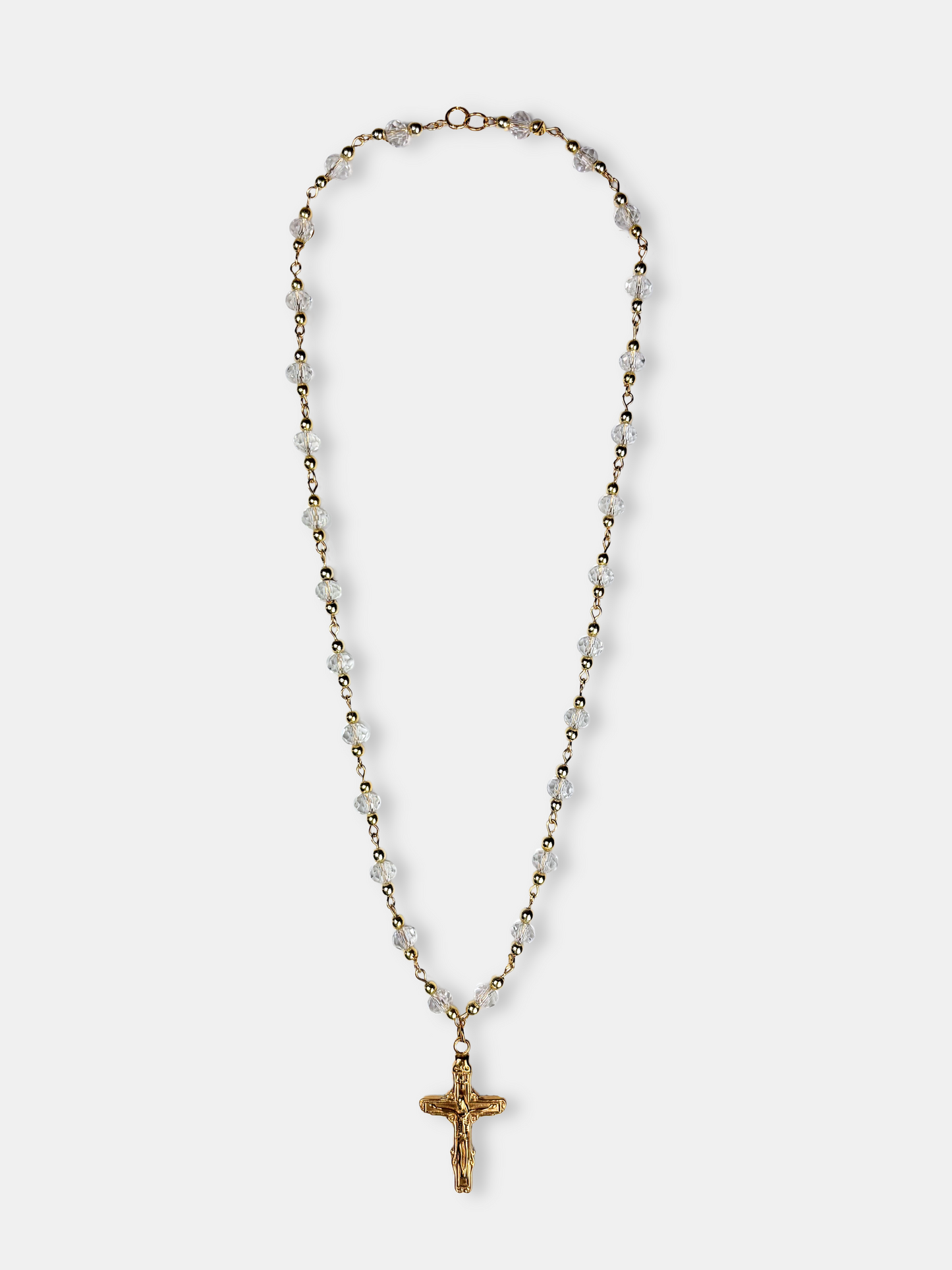Gold rosary-style necklace with clear faceted beads and a detailed cross pendant, blending sophistication with classic design.