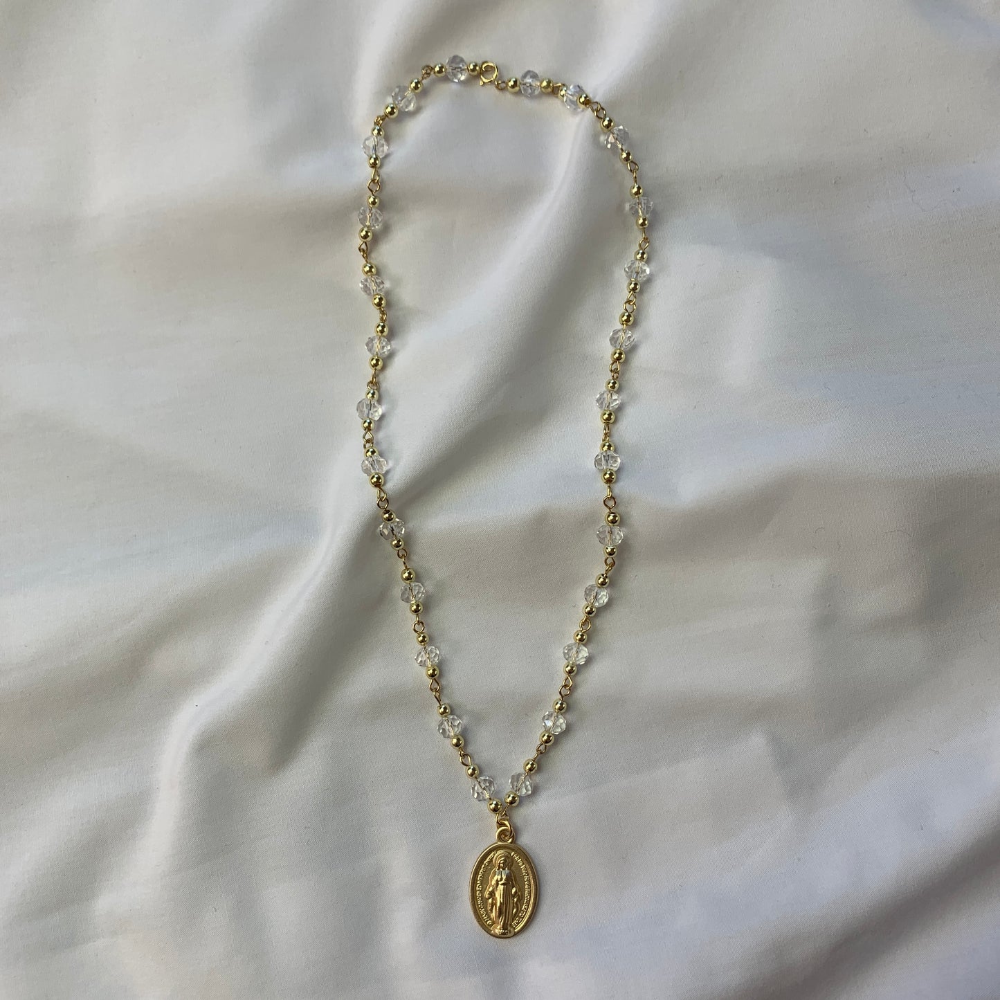Gold and clear crystal necklace with a detailed Virgin Mary medal, symbolizing faith and devotion.
