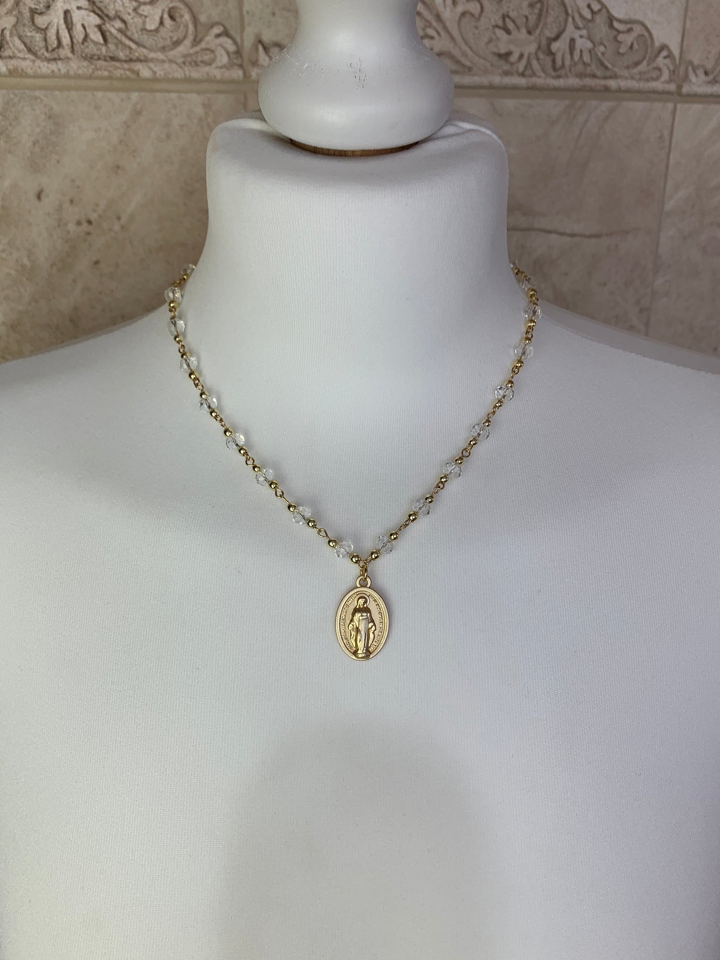 Gold Virgin Mary necklace with clear crystal chain, displayed on a white mannequin.