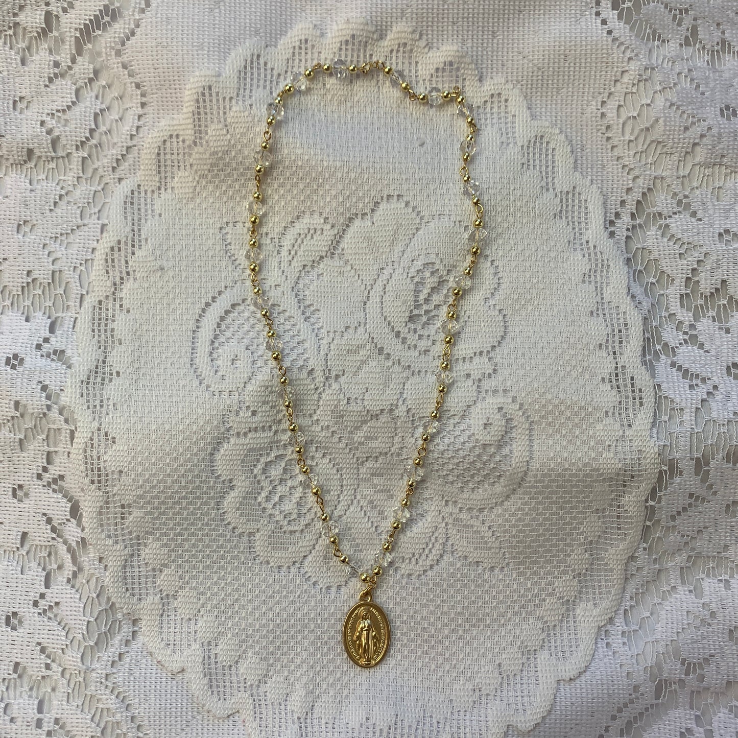 Elegant gold religious pendant featuring the Virgin Mary, suspended from a delicate crystal chain.