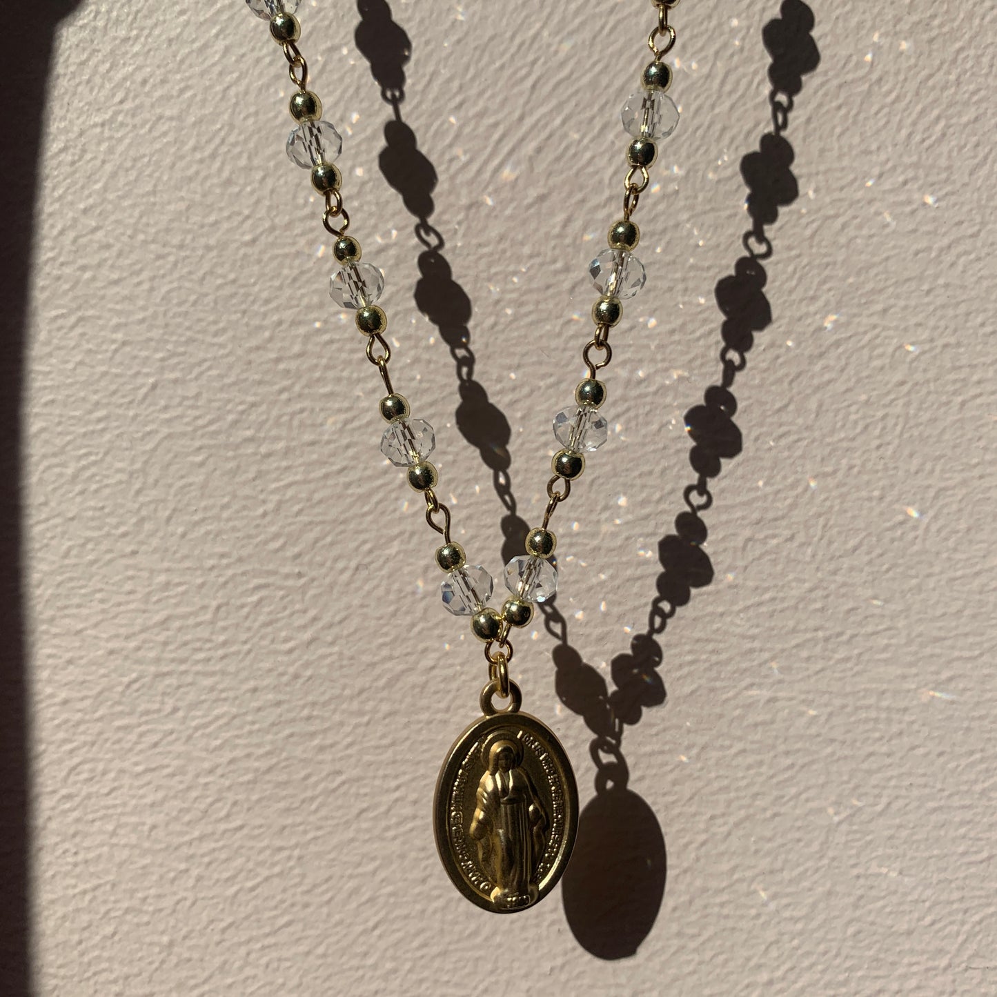 Faithful jewelry piece: a gold Virgin Mary pendant on a dainty clear crystal chain, inspired by spiritual grace.