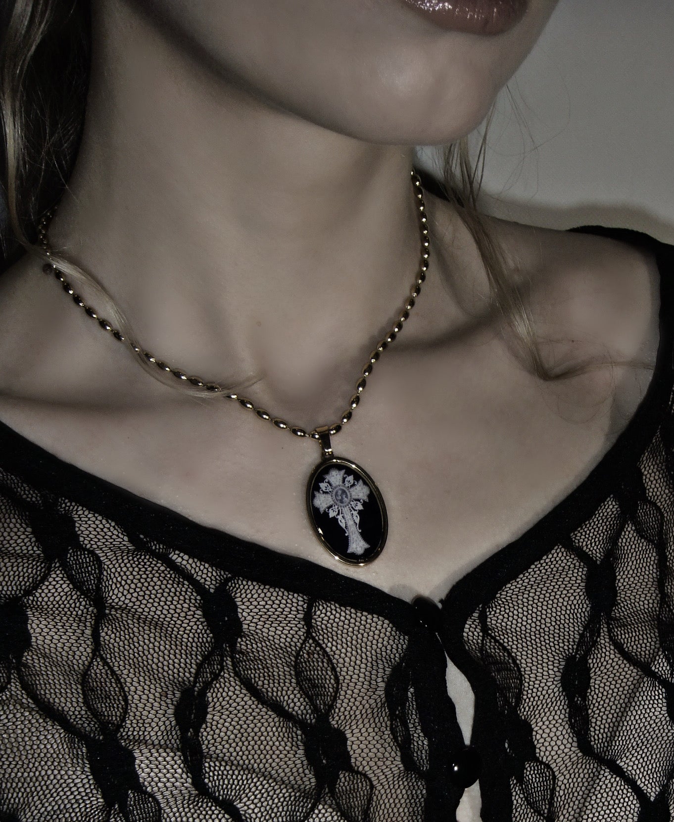 Handmade gold necklace with an oval black pendant featuring an ornate white cross.