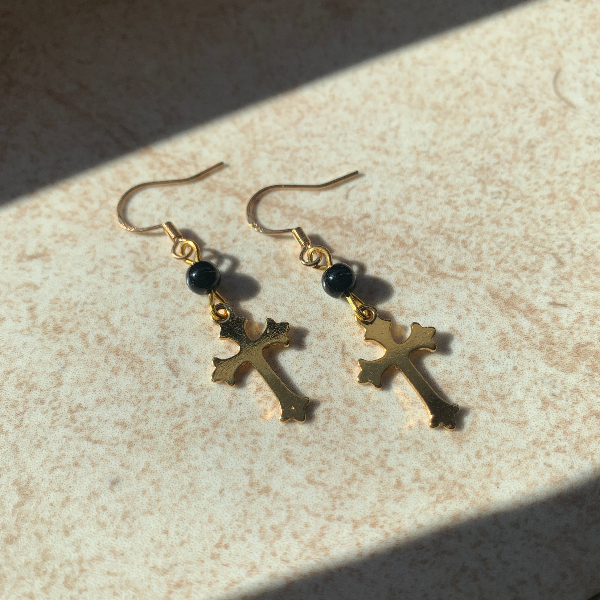 Delicate gold cross drop earrings featuring smooth black beads, perfect for gothic and baroque fashion styles.