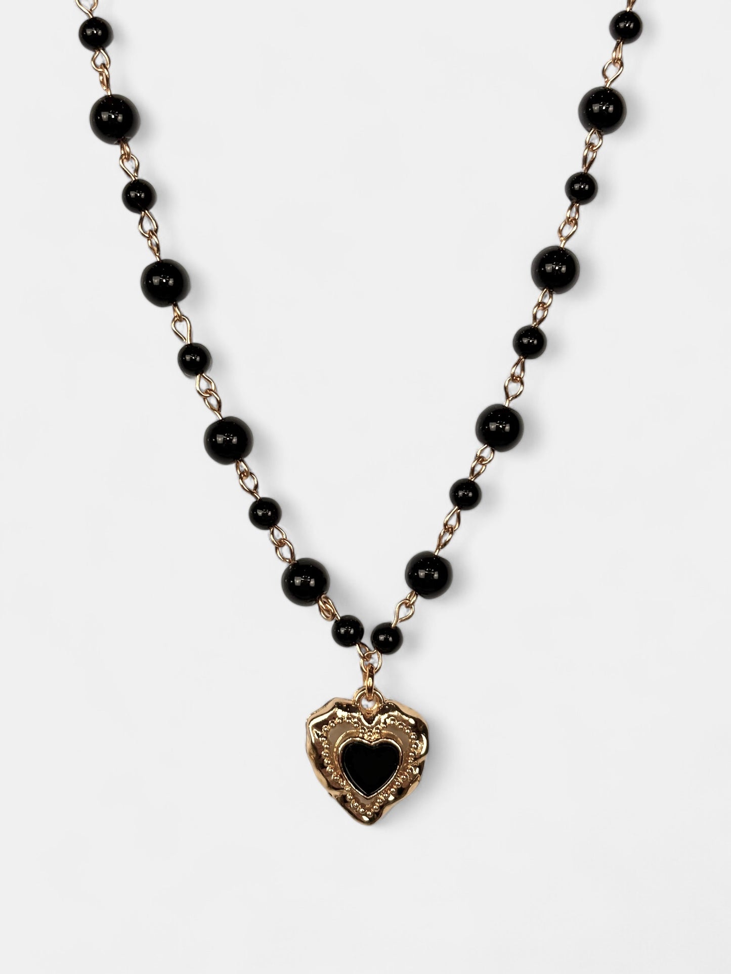 Vintage-inspired gold-plated heart pendant with black enamel detail, hanging from a black onyx bead choker.