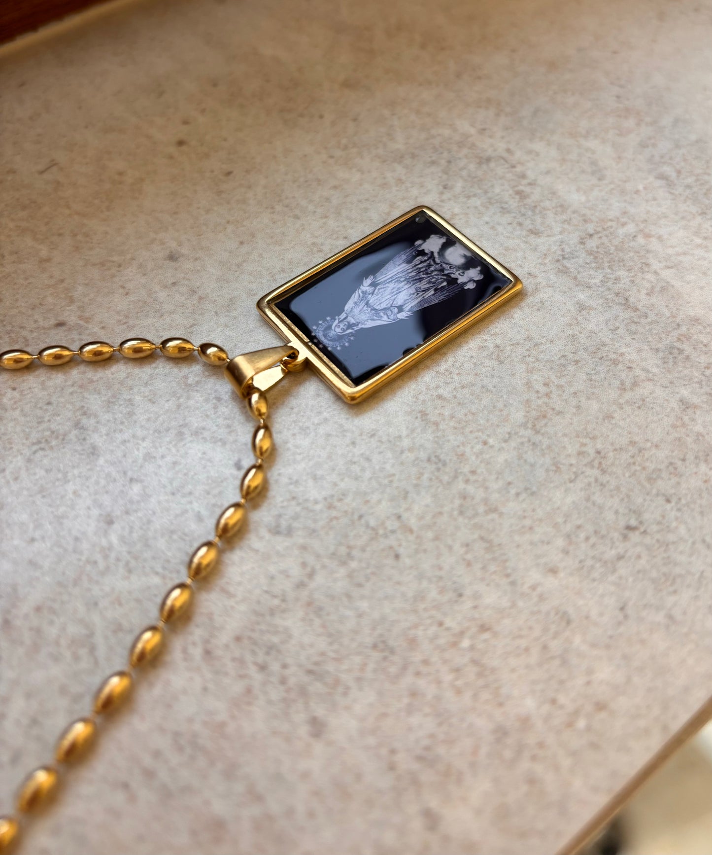 Black and gold necklace with a sacred illustration of the Virgin Mary beneath a glass-like dome.