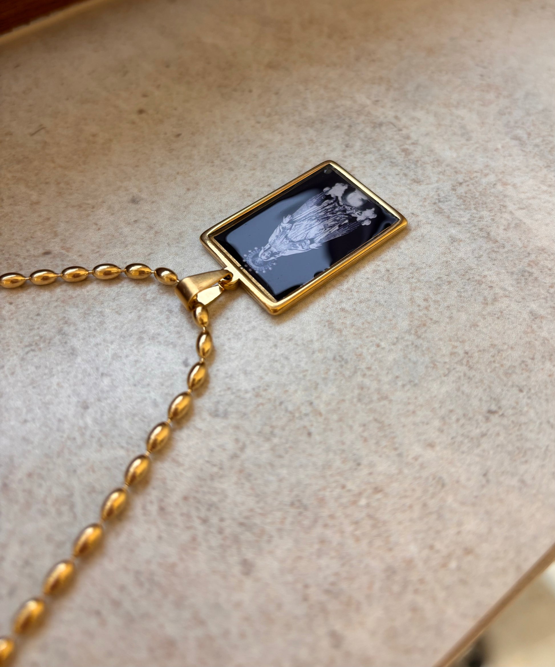 Black and gold necklace with a sacred illustration of the Virgin Mary beneath a glass-like dome.