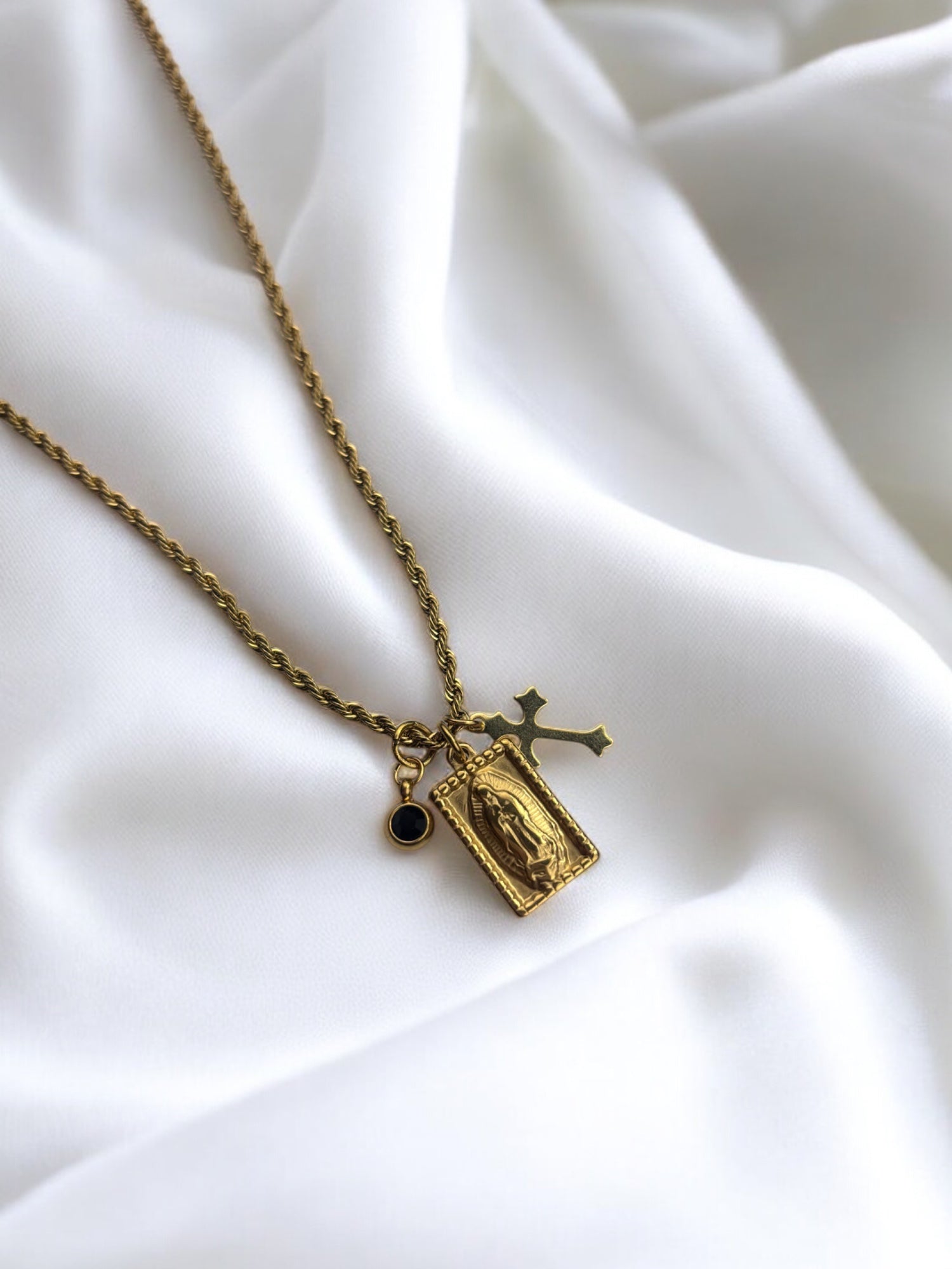 Religious gold pendant necklace with a Virgin Mary medal, gothic-style cross charm, and a delicate black stone, perfect for vintage and faith-inspired jewelry lovers.