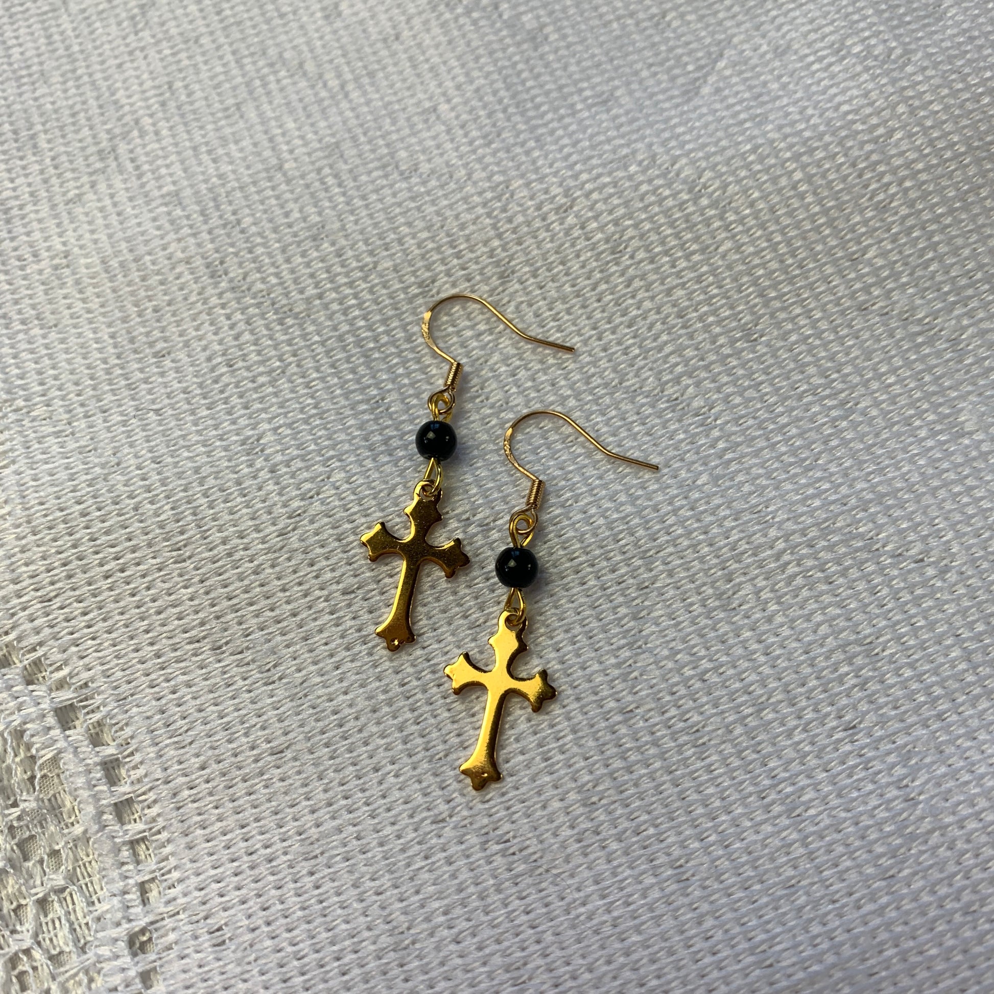 Lightweight gold cross charm earrings with black bead accents, a subtle yet bold statement piece.