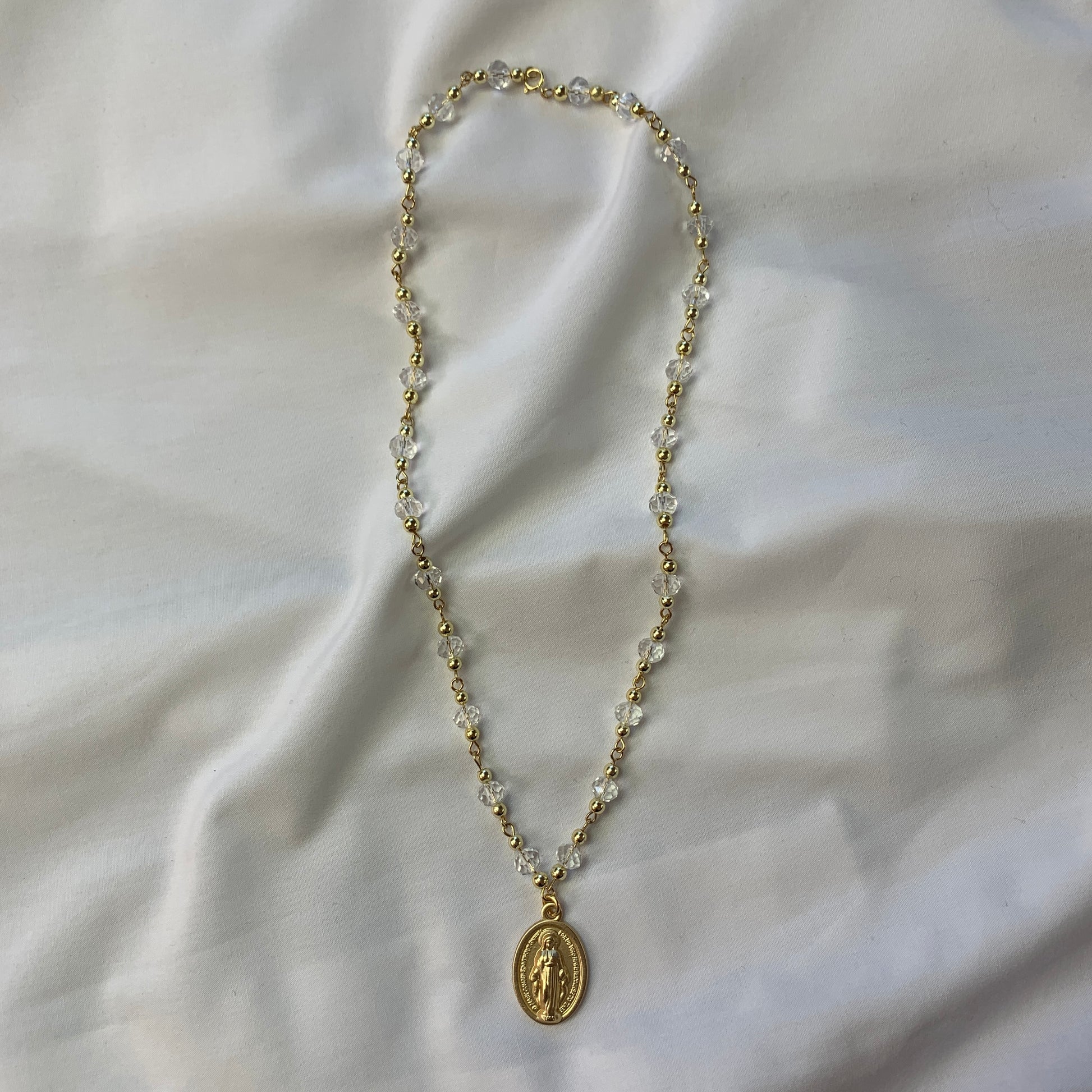 Gold and clear crystal necklace with a detailed Virgin Mary medal, symbolizing faith and devotion.