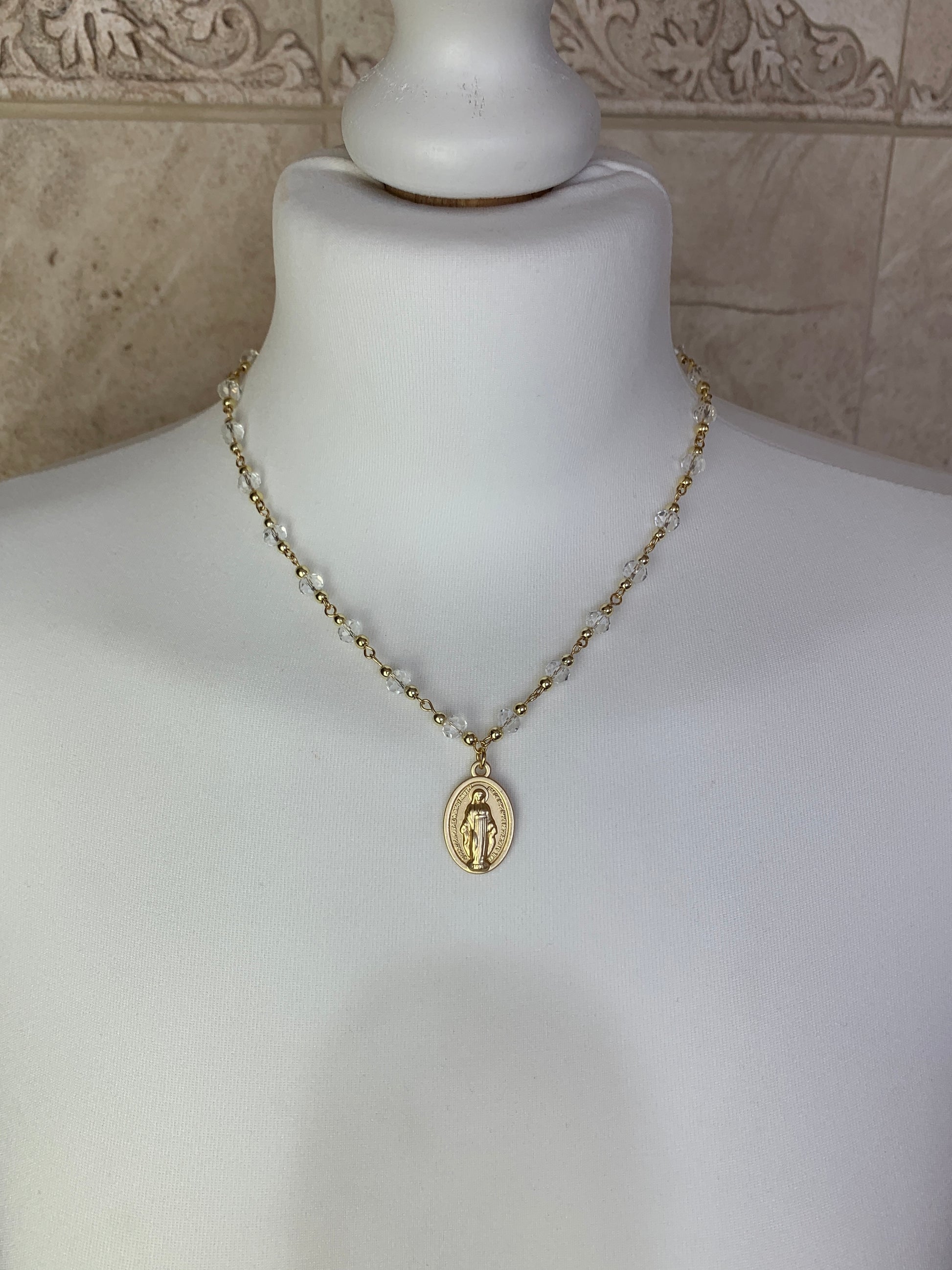 Gold Virgin Mary necklace with clear crystal chain, displayed on a white mannequin.