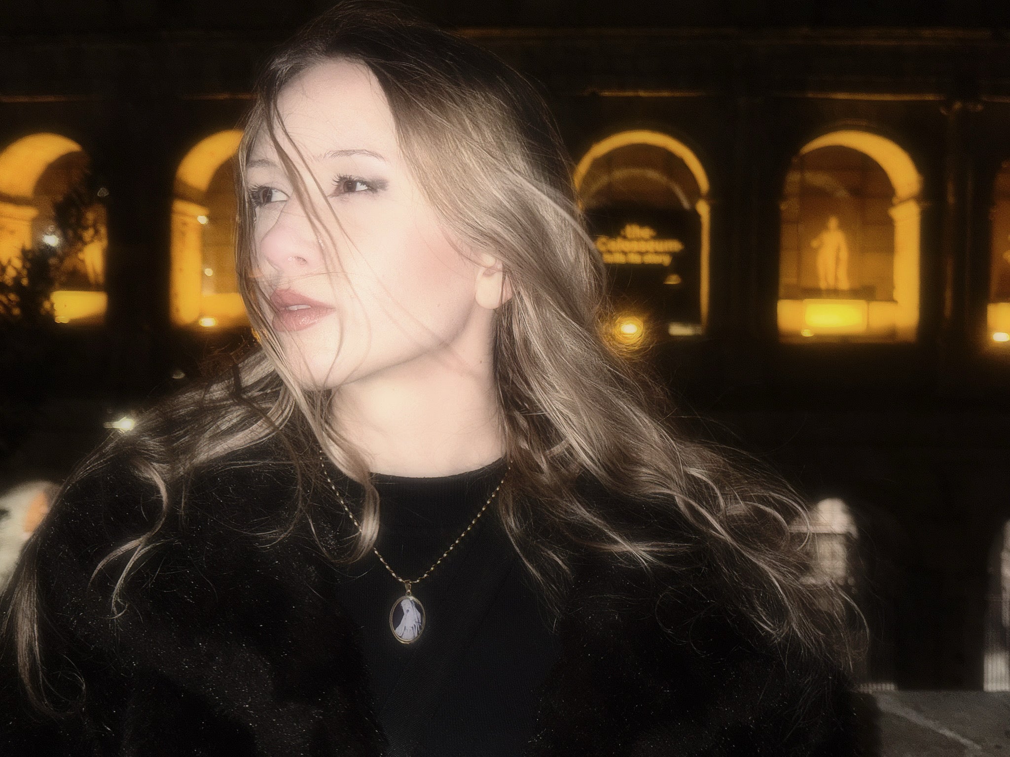 Girl standing in front of a Colosseum in Rom showcasing a gold medallion.