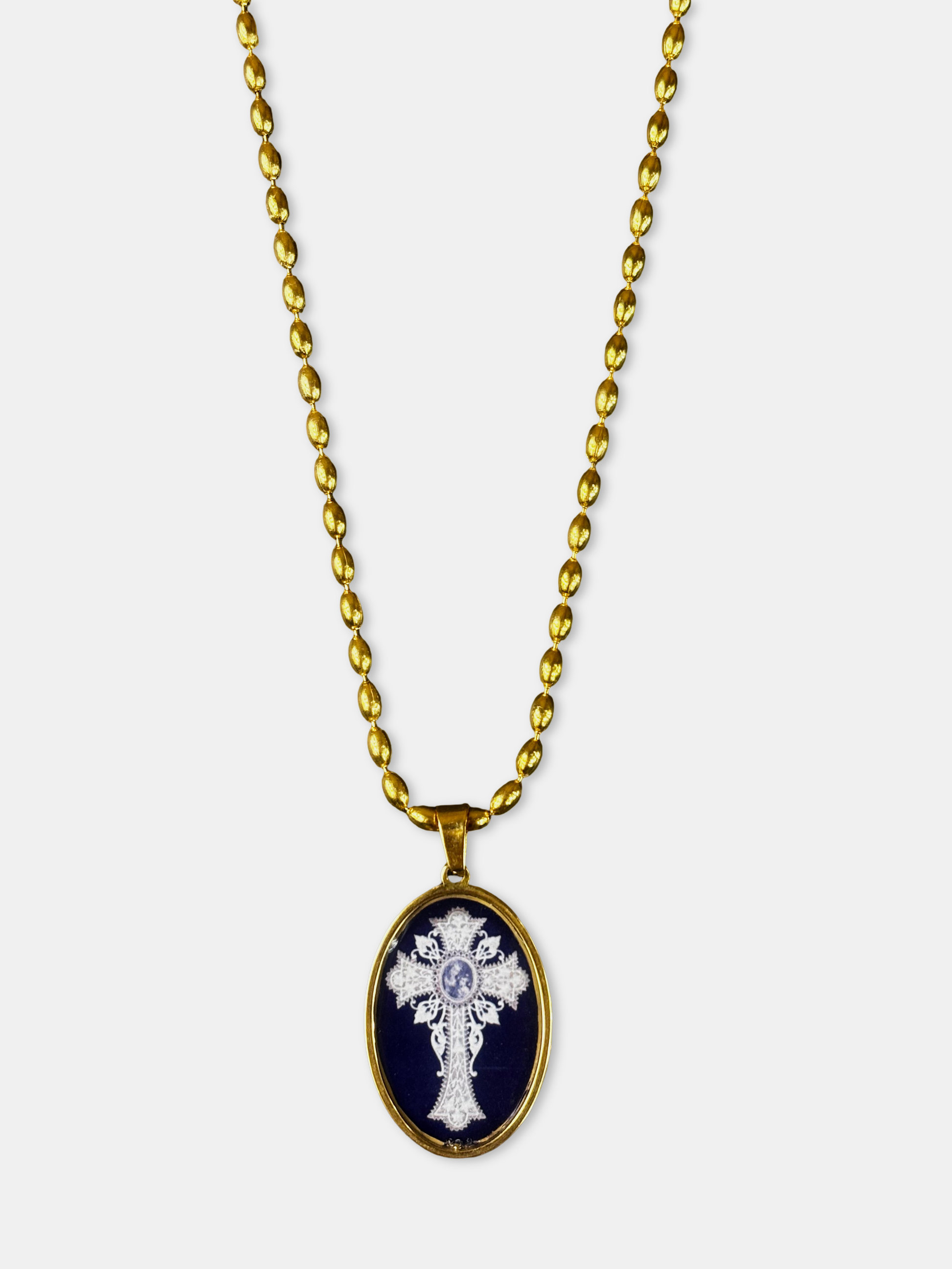 Artistic gold necklace with oval pendant and delicate cross illustration beneath a glass-like dome.