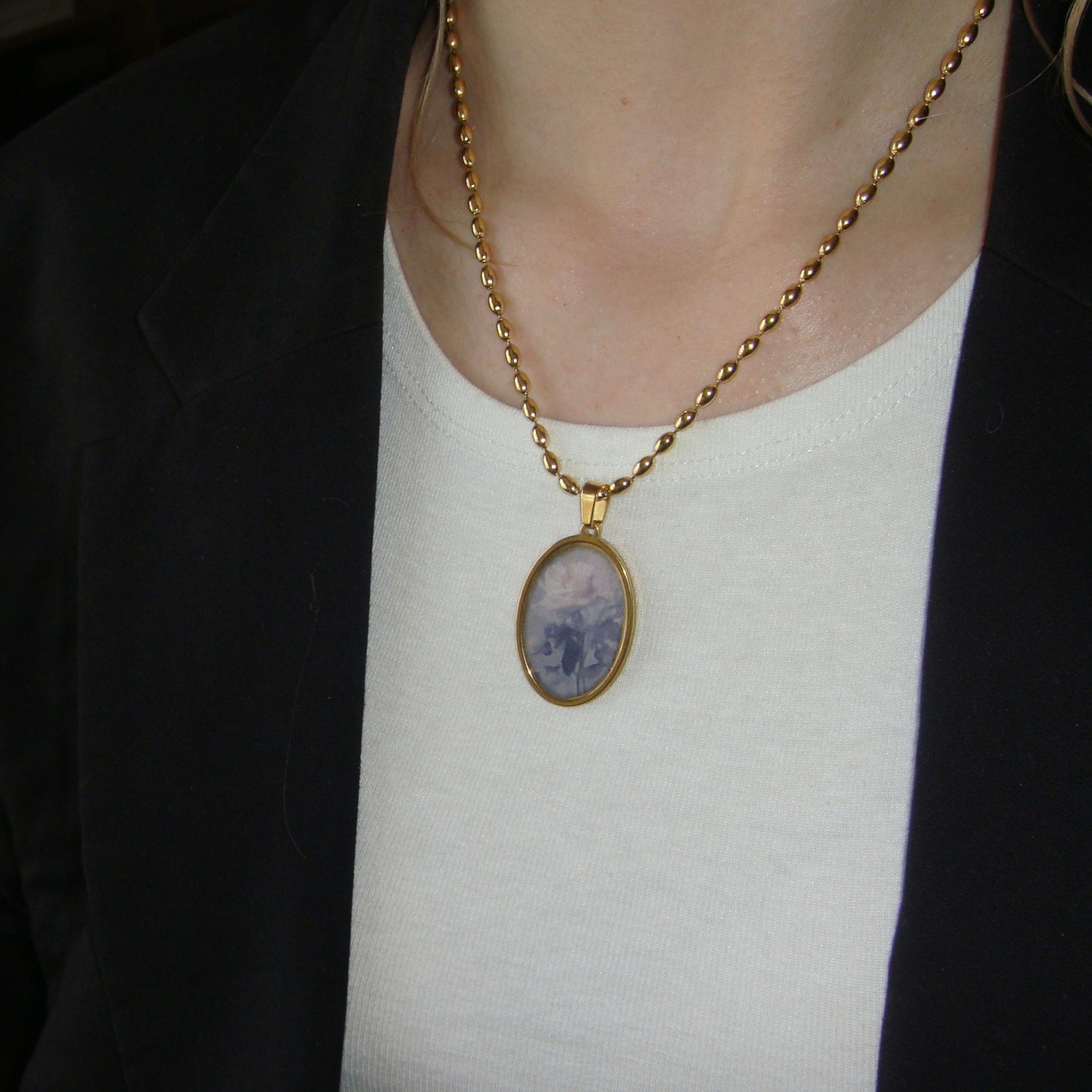 Romantic gold necklace with oval pendant, featuring a faded rose artwork.